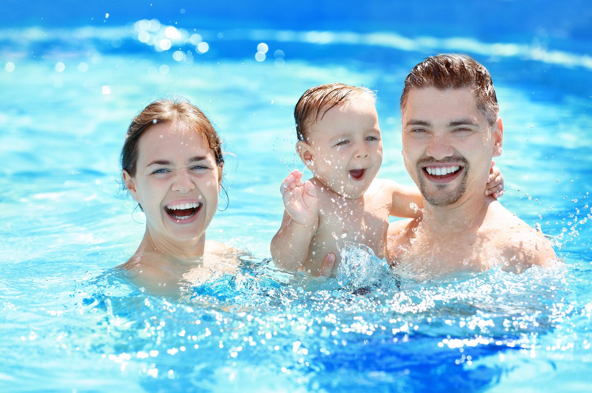 Kleiner Junge, der mit Eltern im Pool Spaß hat undschwimmen lernt.