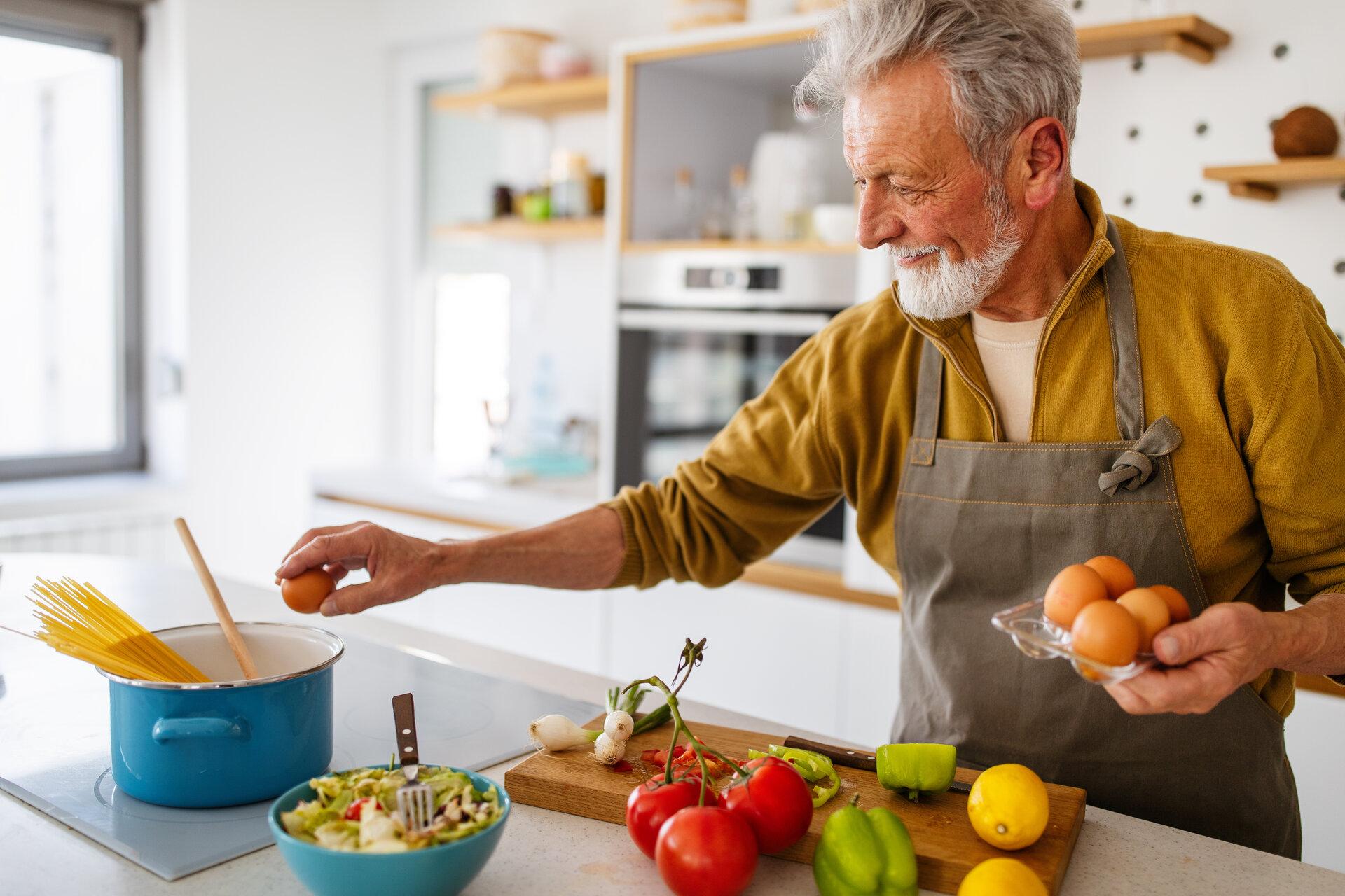 Glücklicher Rentner, der in der Küche kocht. Ruhestand, Hobby Menschen Konzept