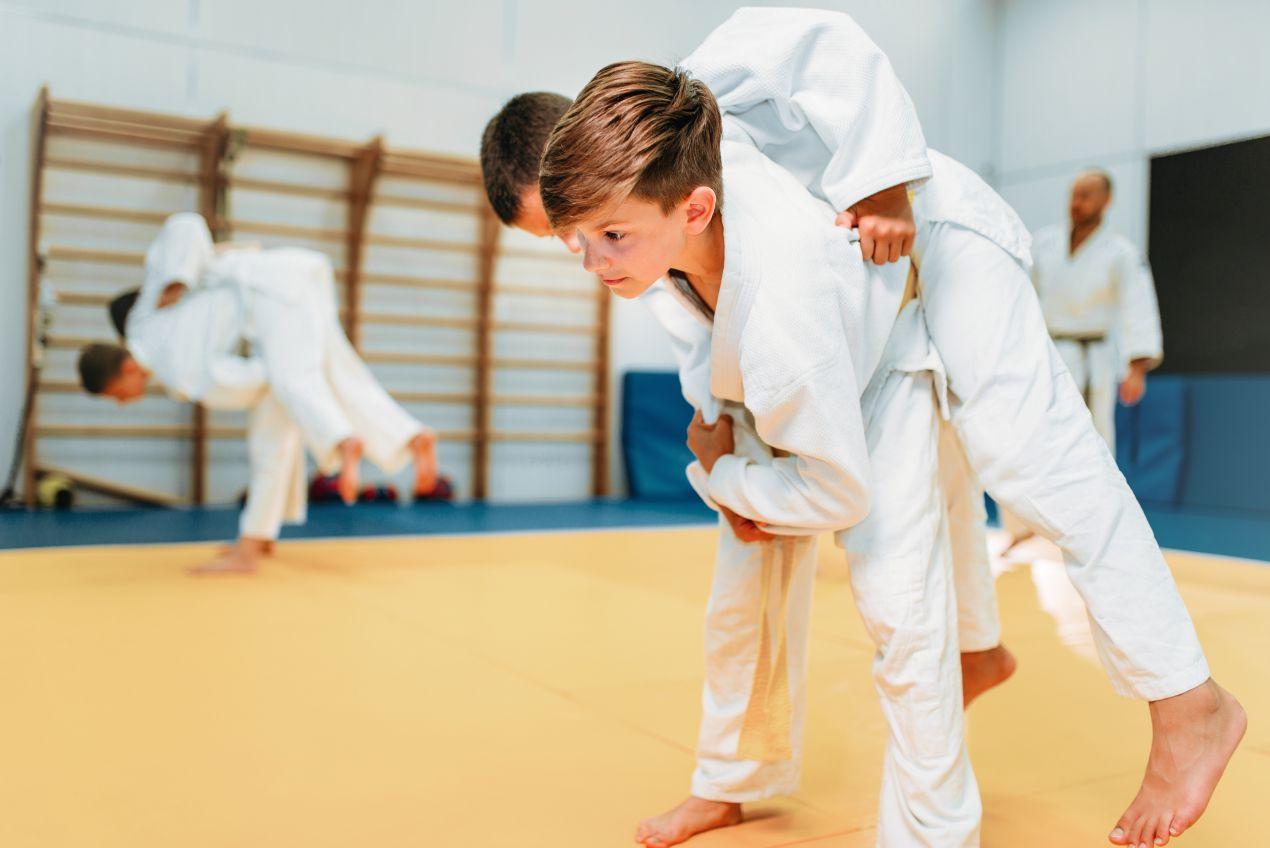 Kind in Karateanzug fuehrt Wurftechnik mit Trainingspartner aus, intensives Kindertraining in Karatekurs in Muenchen