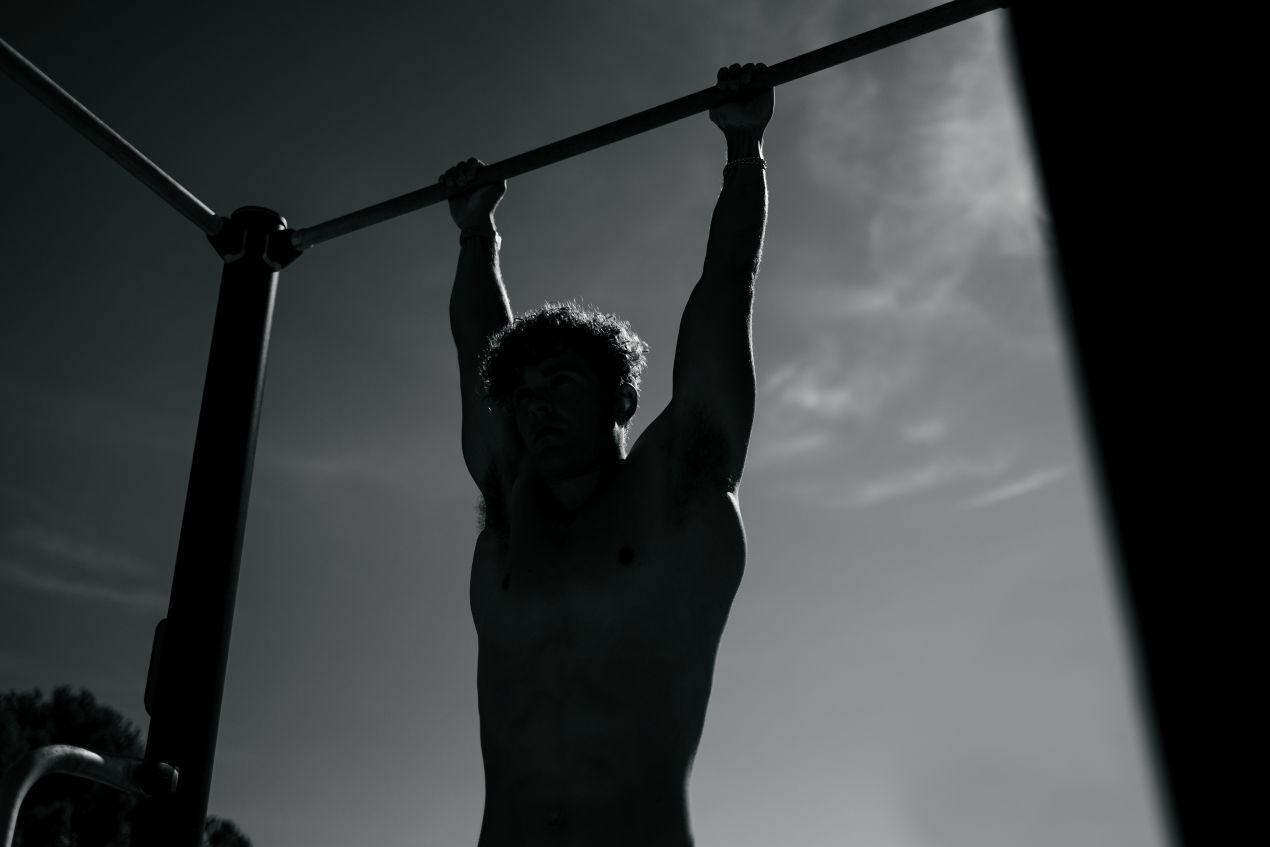 Mann haengt an Klimmzugstange beim Calisthenics Training im Freien, aufgenommen in Schwarzweiss