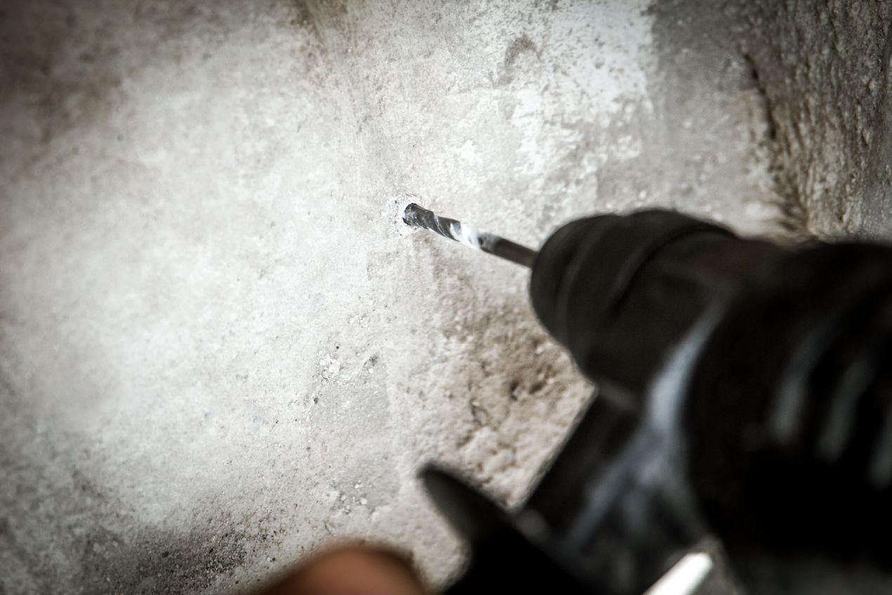 Bohrmaschine erstellt ein Loch in Beton als Vorbereitung fuer das Eindrehen von Betonschrauben in Bauprojekten