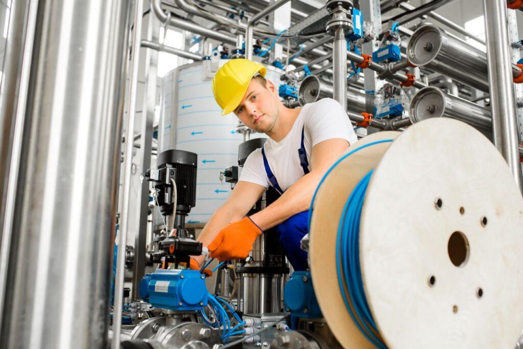 Facharbeiter installiert Maschinenkomponenten in einer Industrieanlage und verwendet Betonschrauben fuer sichere Verankerung